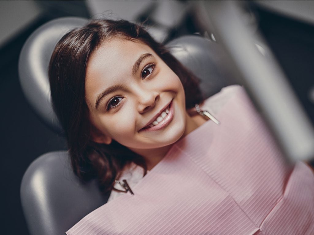 A young girl smiling in a chair at a pediatric dental office.