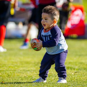 A toddler playing with a football without a mouthguard.